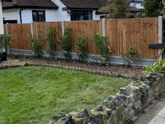 New fence run on concrete posts behind a lawn and stone wall